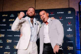Conor McGregor in a white suit does a fist pump as David Feldman smokes a cigar at the BKFC press conference