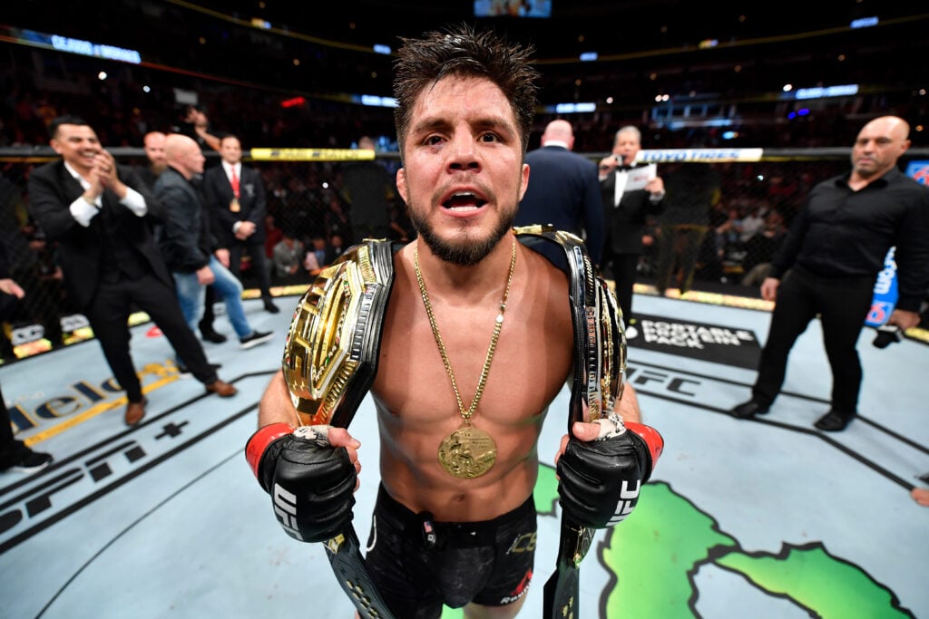 Henry Cejudo poses with his two UFC titles after defeating Marlon Moraes at UFC 238