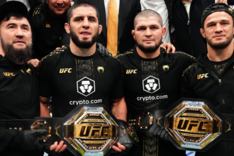 Islam Makhachev and Khabib Nurmagomedov, flanked by Usman Nurmagomedov and their coach, holding Makhachev's two UFC belts