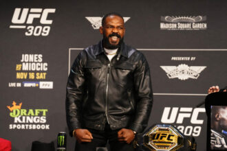 Jon Jones poses on stage at the UFC 309 press conference