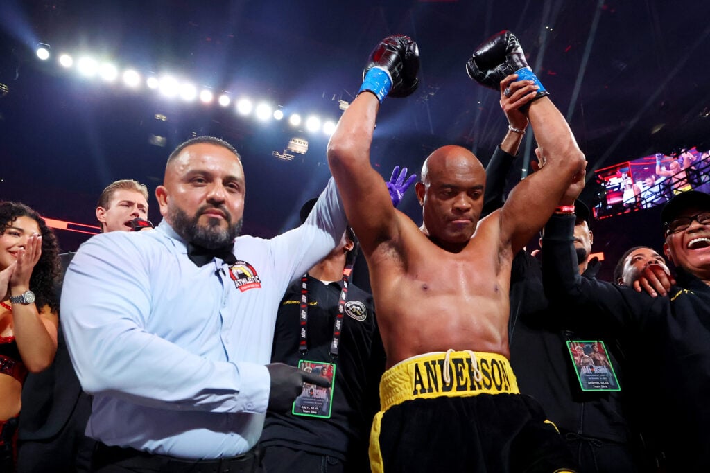 Anderson Silva, wearing black and gold trunks with his first name embroidered on the beltline, has his hand raised by the referee after winning a boxing match.